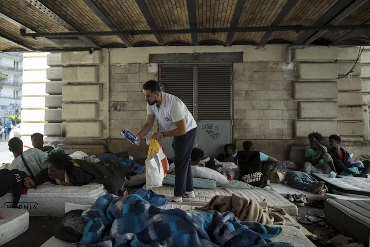 Un bénévole de l’ONG Médecins du monde (MdM) distribue des bouteilles d’eau pour faire face aux fortes chaleurs lors d’une maraude dans le camp de migrants du quartier Stalingrad à Paris, le 12 juillet 2023