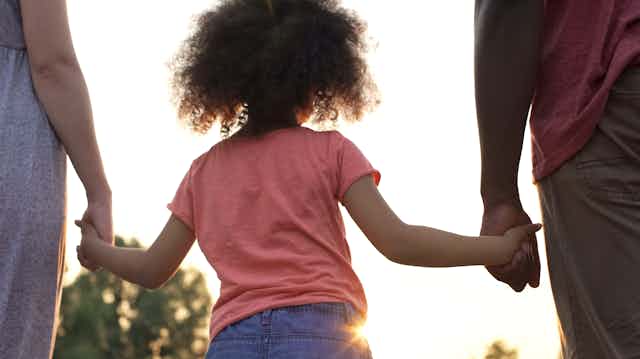 Child seen from behind holding parents' hands