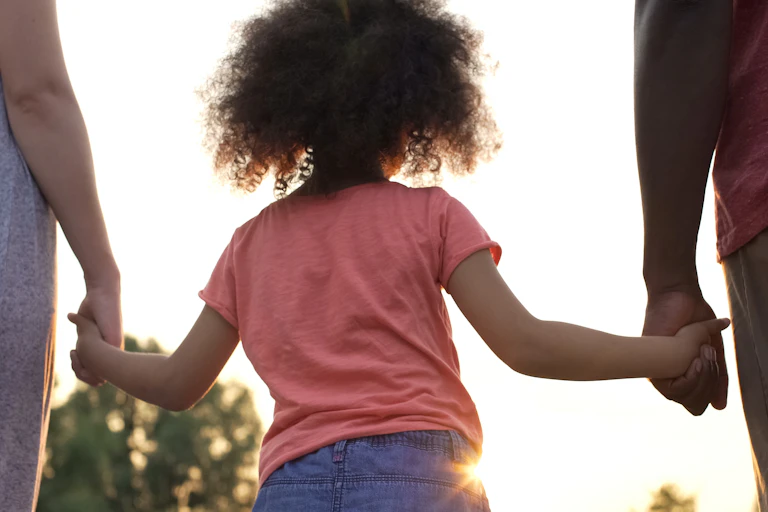 Child seen from behind holding parents' hands