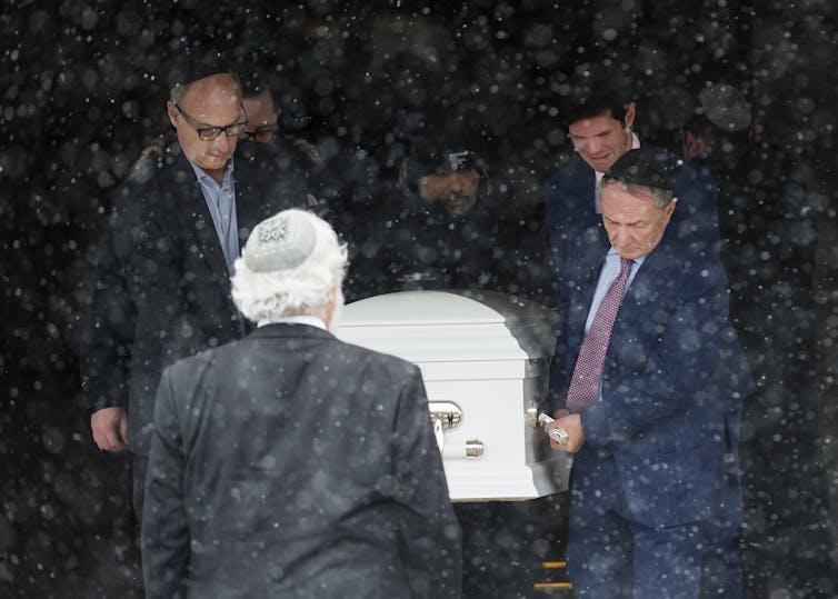 Four men carry a white casket, one openly weeping.