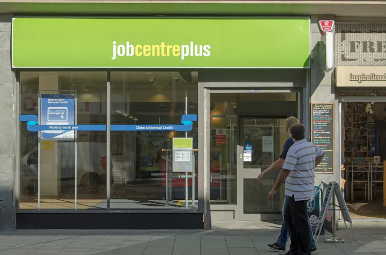 Two men stand on the pavement outside of a JobCentrePlus