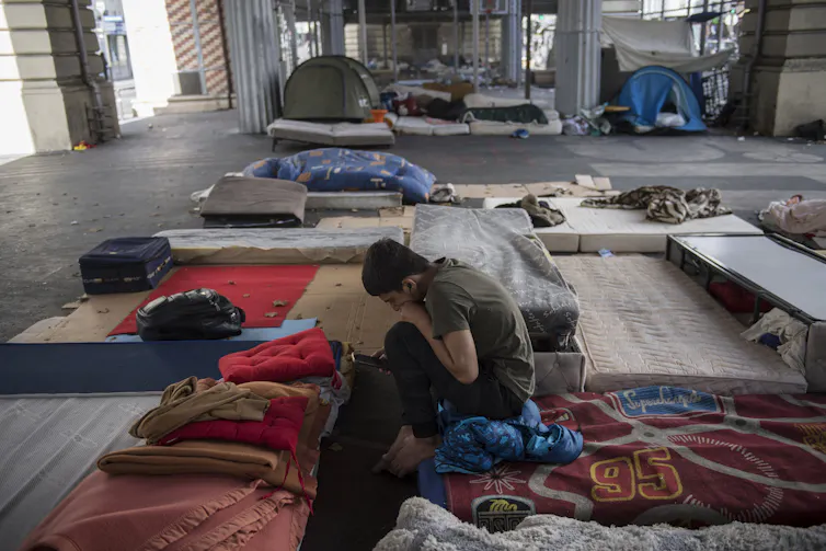 Un homme sur son matelas regarde son téléphone dans le camp de migrants du quartier Stalingrad à Paris, le 12 juillet 2023