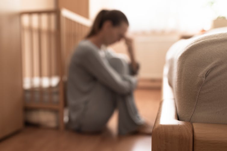 Out-of-focus image of exhausted woman sitting on the floor beside a crib
