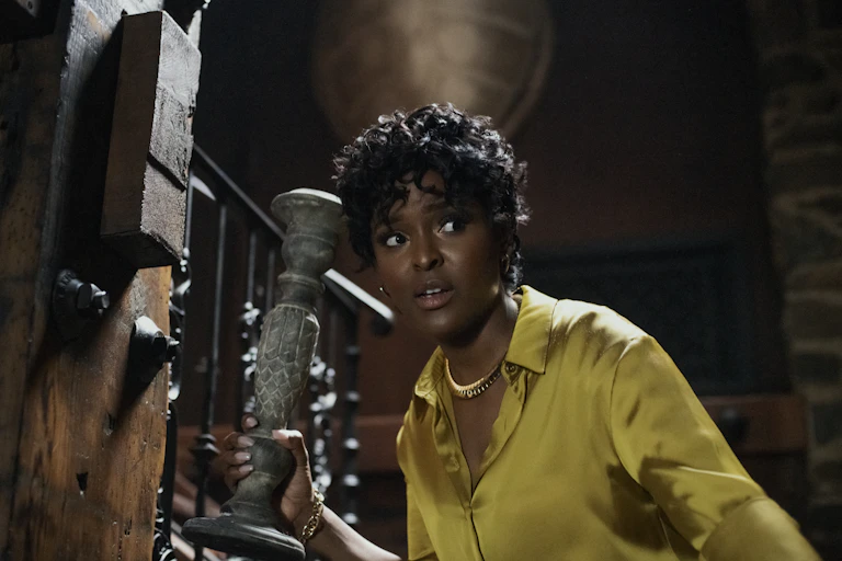 Antoinette Robertson as Lisa in The Blackening holding a candlestick and wearing a yellow silk blouse.