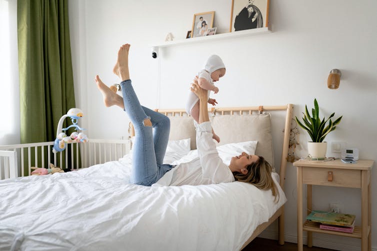 Woman lying on a bed with baby in the air.