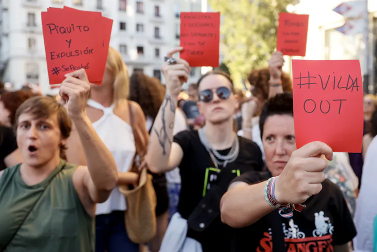 Close up of marching protesters holding up red cards with messages written on them in Spanish, calling for the firing and resignation of Spanish football officials