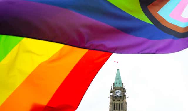 Rainbow flags wave in front of the Canadian parliament building.