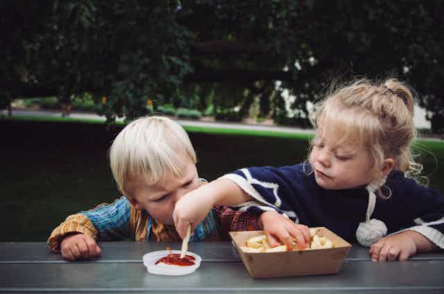 Children eating chips at a park bench