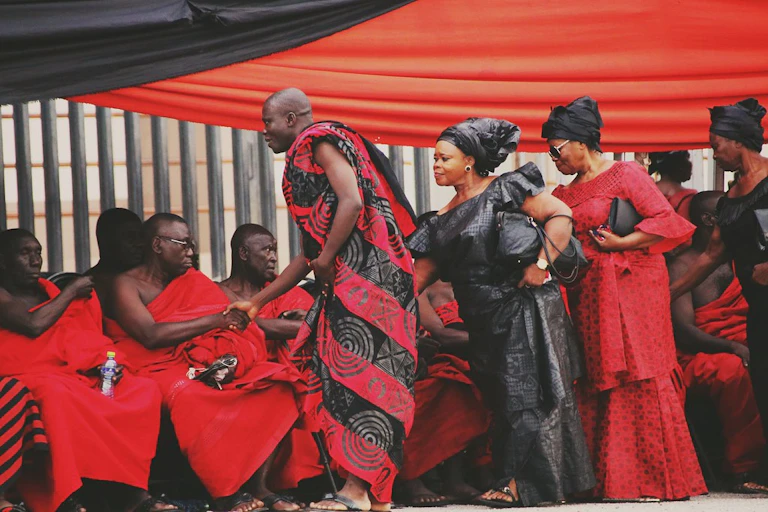 Men and women in red and black cloth shake hands.