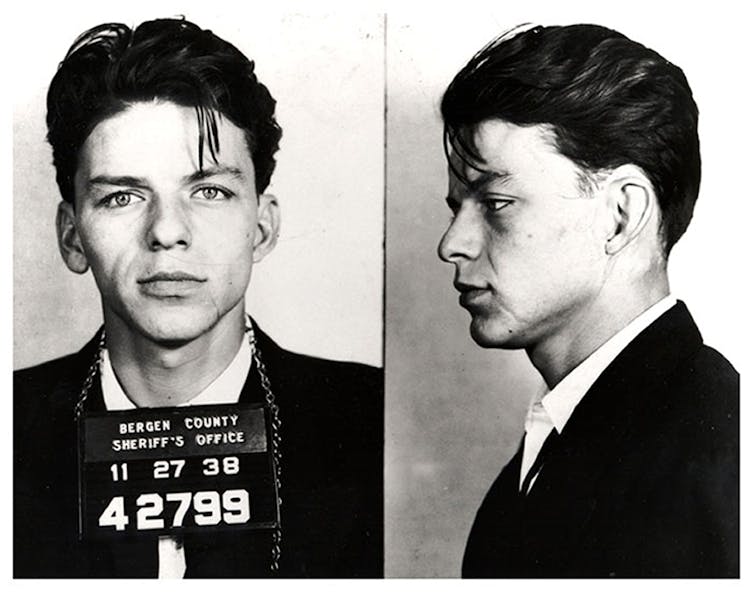 A young Frank Sinatra looks directly at the camera with a Bergen County Sheriff's office plate around his neck with numbers.