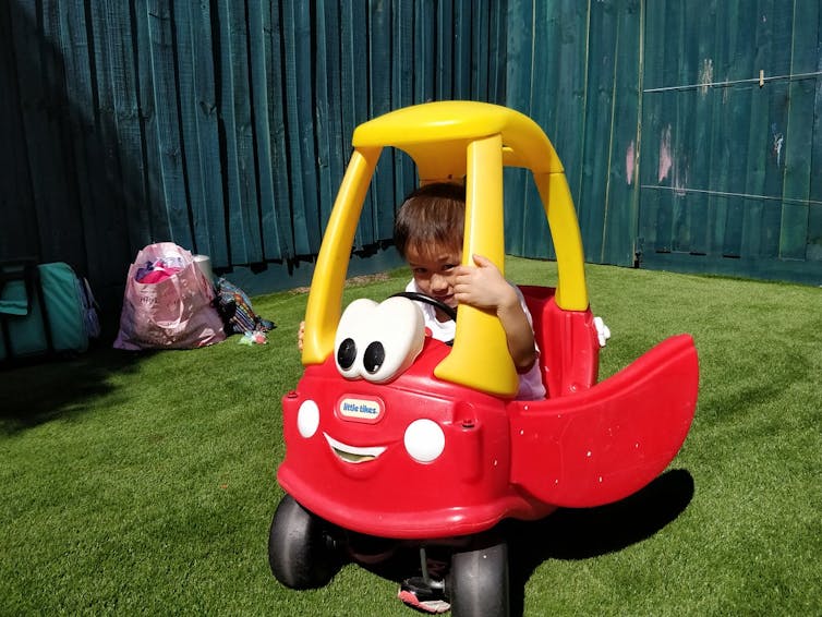 A child smiles from within a Cozy Coupe car.