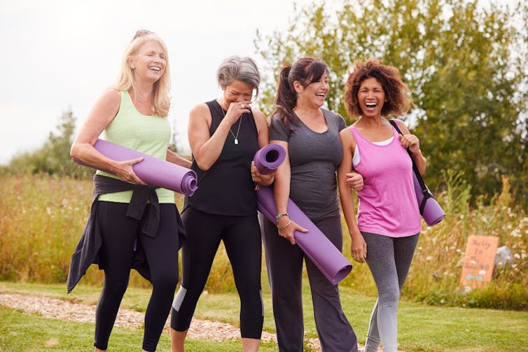 Group of women of different ages with yoga mats walking through a park.