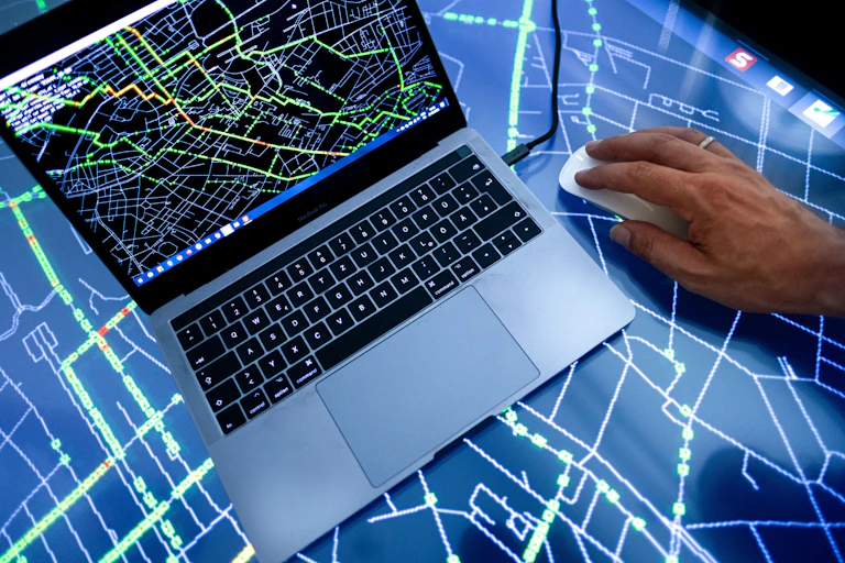 A laptop computer displaying a map with colored lines sitting on a large table top computer display showing the same map