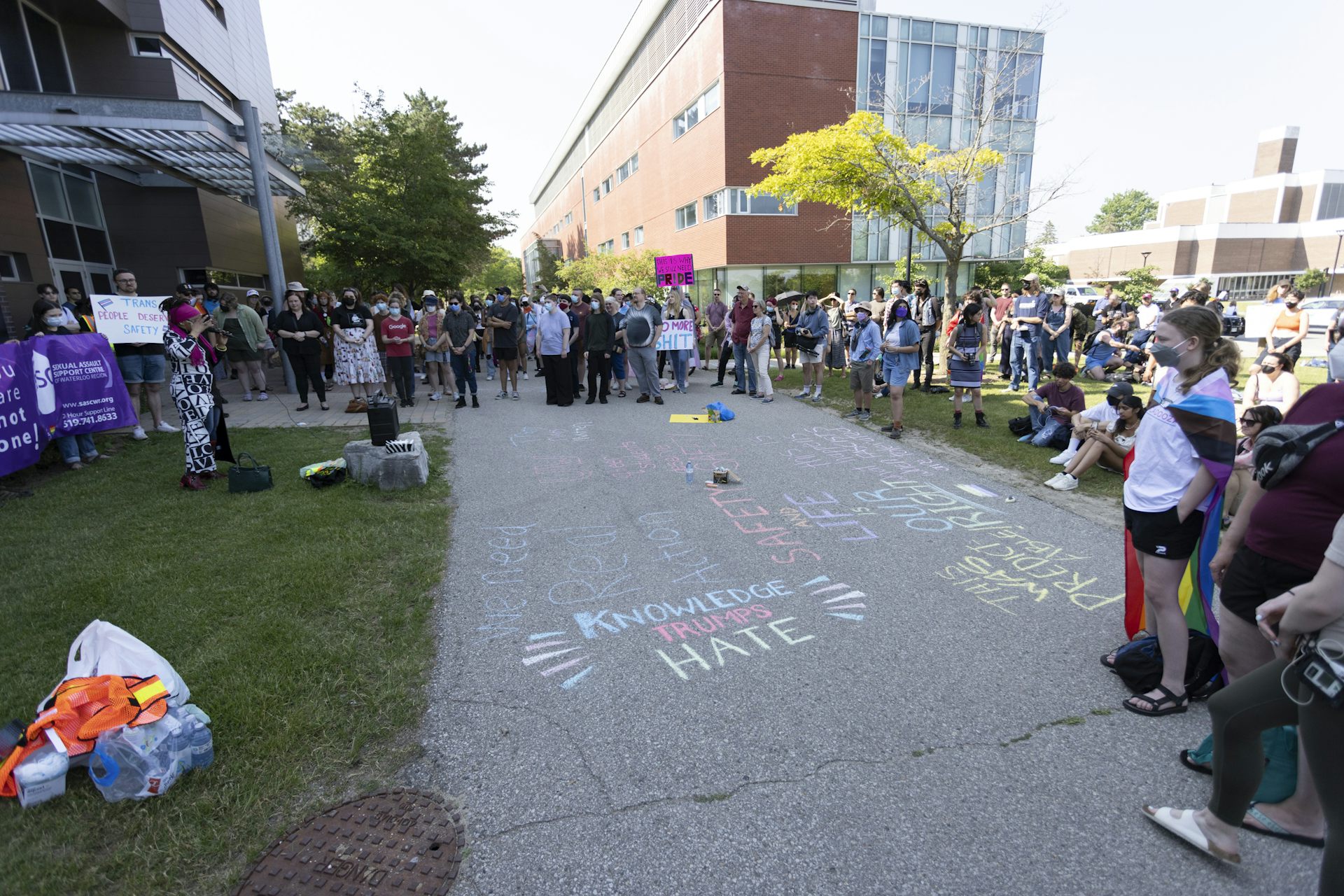 People gather in a circle around chalk writing on the ground that says knowledge trumps hate.