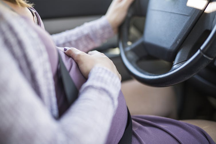 Pregnant woman driving, holding belly