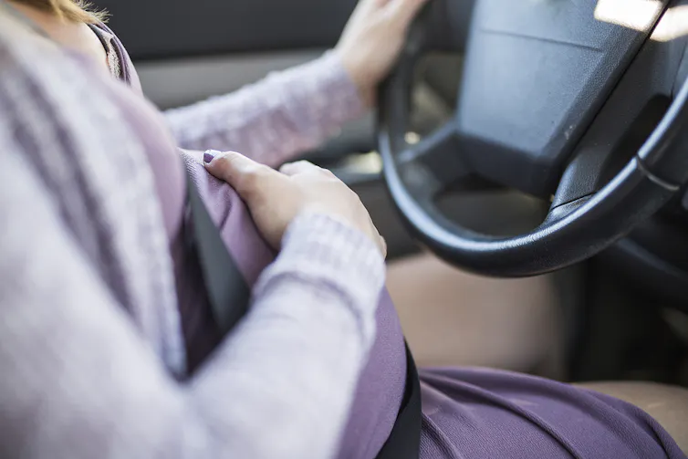 Pregnant woman driving, holding belly