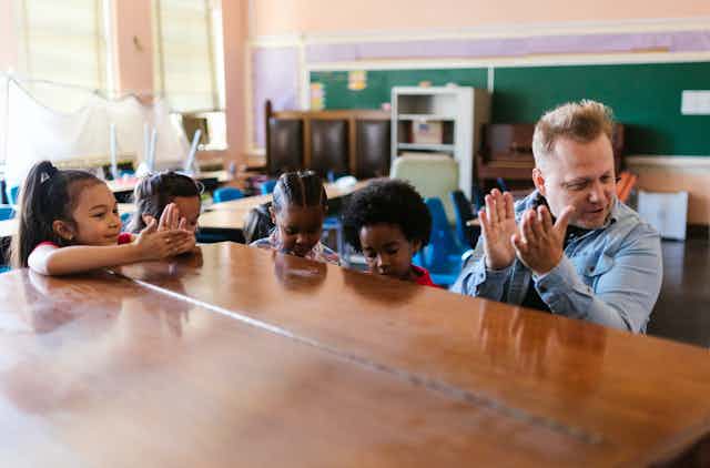 Man sits at a piano with four children in a classroom 