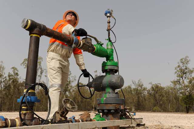 A worker turns a valve on a coal seam gas well head near Chinchilla, central Queensland