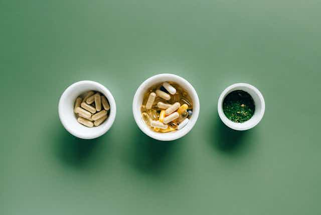 Three white bowls of supplements in a row against green background