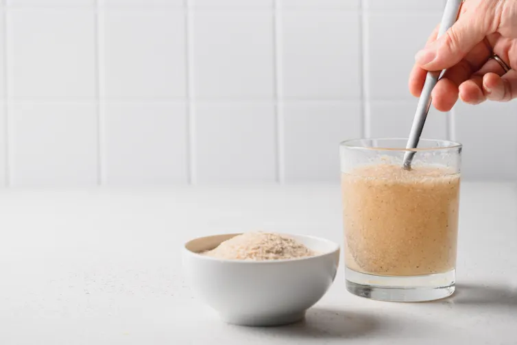 Person stirring in psyllium into glass of water, bowl of psyllium next to glass