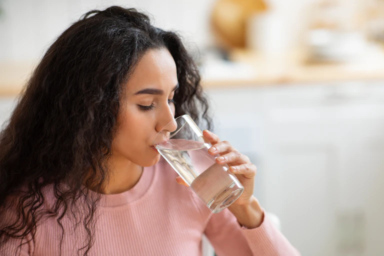 A young woman drinks a glass of water.