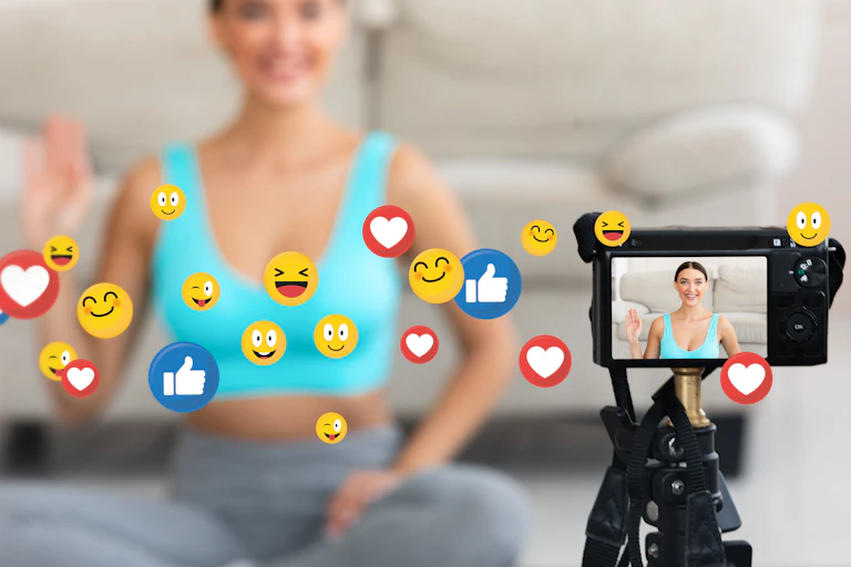 Woman in blue crop top with hand raised (blurred out) camera in foreground focussed on women and surrounded by emojis.