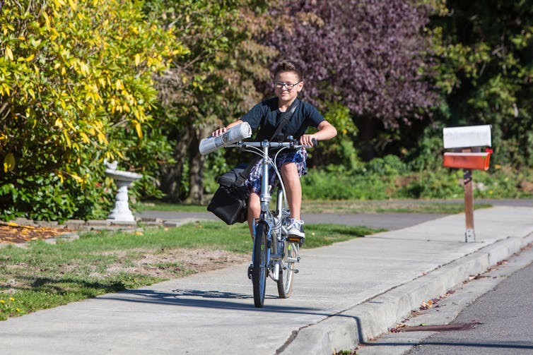 A boy on a bike delivering a newspaper.