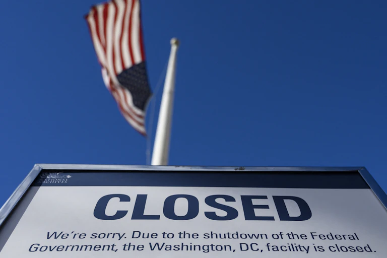 A "closed" sign is displayed on a government building during the US government shutdown in December 2018. An American flag is visible in the distance.