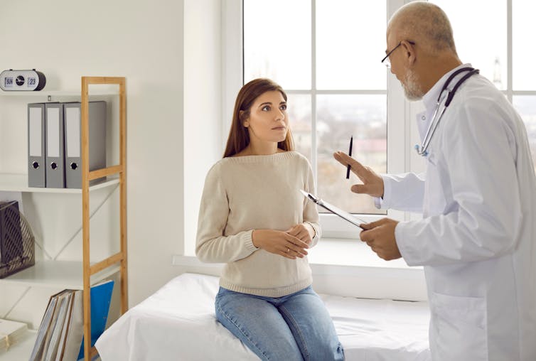 An older male doctor speaks with a young female patient.