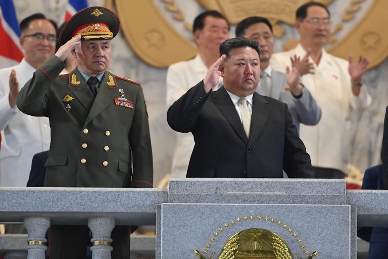 Russian defence minister Sergei Shoigu stands on balcony next to North Korean lader Kim Jng-un as they both salute a military parade