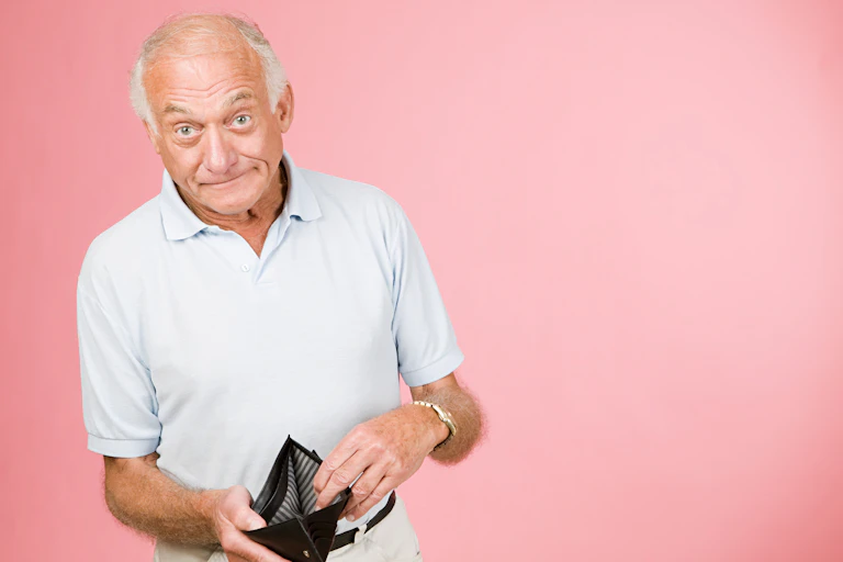 A man with a chagrined expression displays an empty wallet.