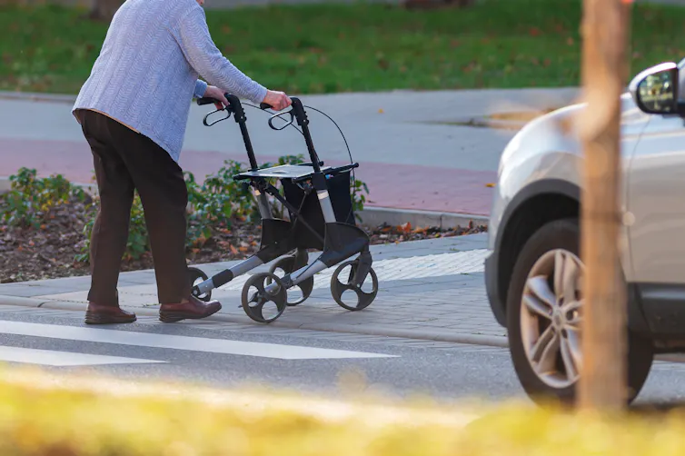 An eldery woman using a walker crossing a street.