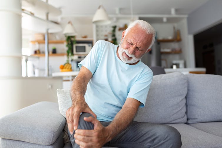 An elderly man holding his knee with a pained look on his face.