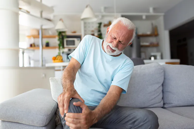 An elderly man holding his knee with a pained look on his face.