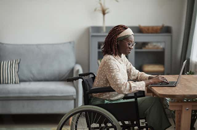 a black woman in a wheelchair siting at a desk working on a laptop.