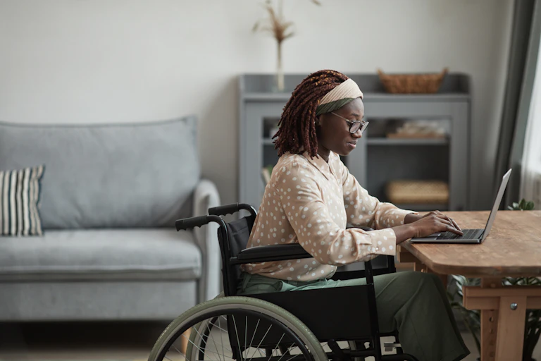 a black woman in a wheelchair siting at a desk working on a laptop.