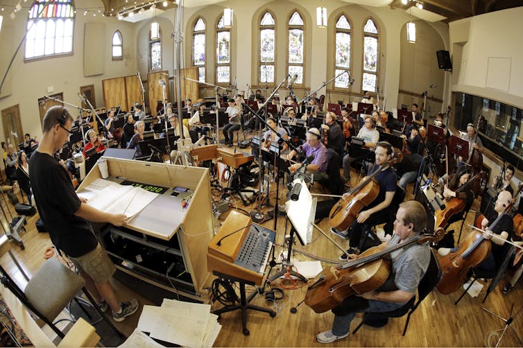 An orchestra seated in a recording studio.