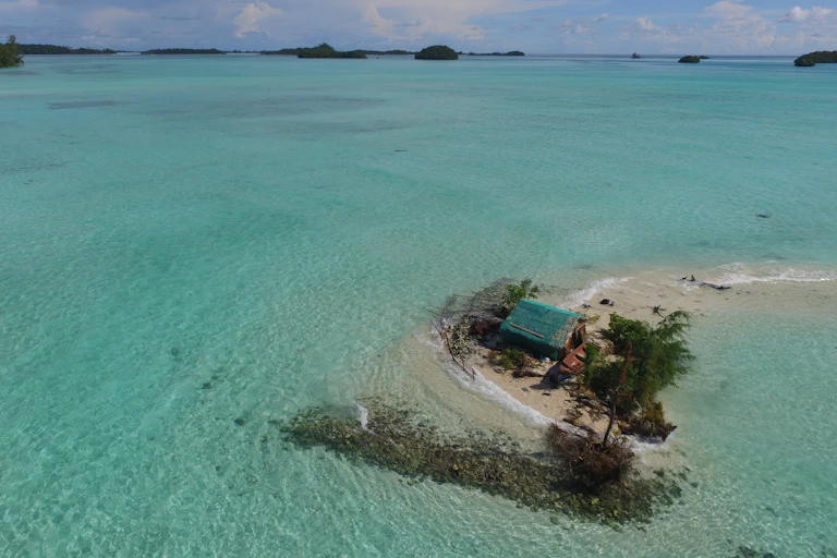 Fotografia aérea mostrando a água do mar cercando uma cabana e árvores em uma pequena ilha, para ilustrar o impacto do aumento do nível do mar nas Ilhas Salomão