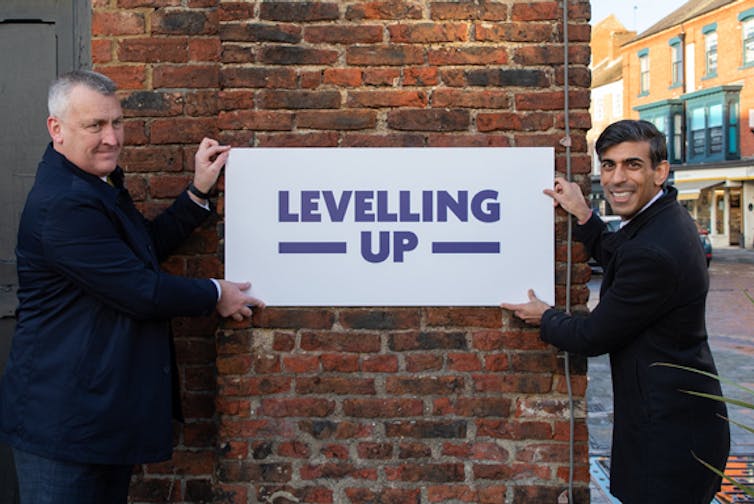 Two men in suits holding up 'Levelling Up' street sign