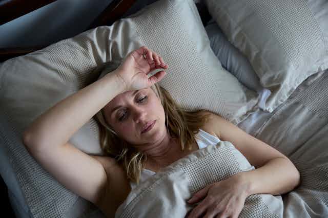 woman lies in bed, looks hot and uncomfortable