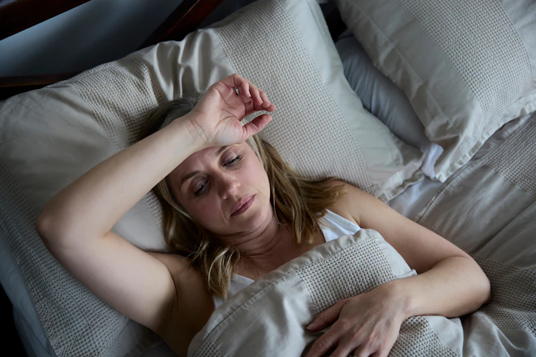 woman lies in bed, looks hot and uncomfortable