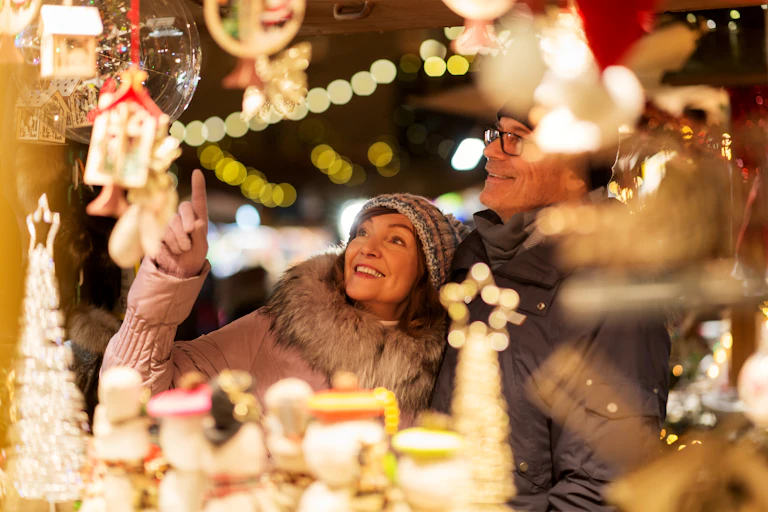 A middle aged couple smiles and points at items in a Christmas display, they are surrounded by out of focus glowing decorations