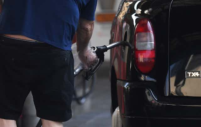 A person inserting a petrol or diesel pump into the side of a black car.