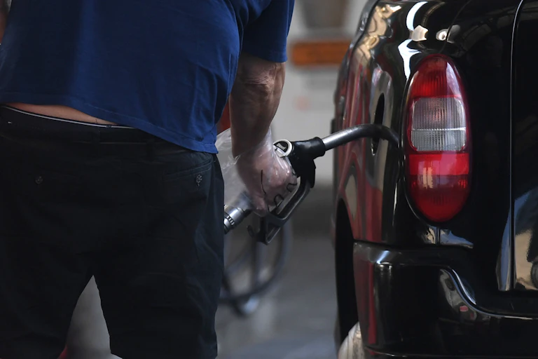 A person inserting a petrol or diesel pump into the side of a black car.