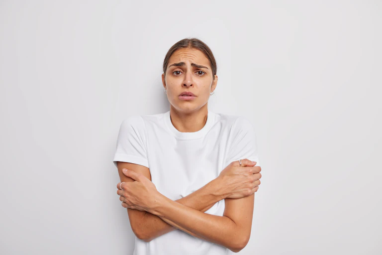 A young woman holds her arms as she shivers.