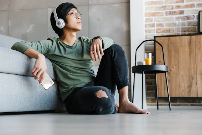 A young asian man wearing large over ear headphones, sat on the floor.