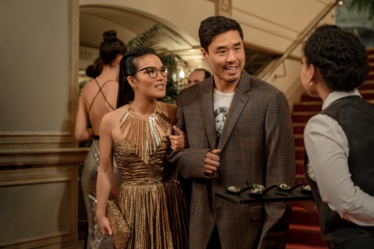 Ali Wong and Randall Park smile and link arms at a fancy event.
