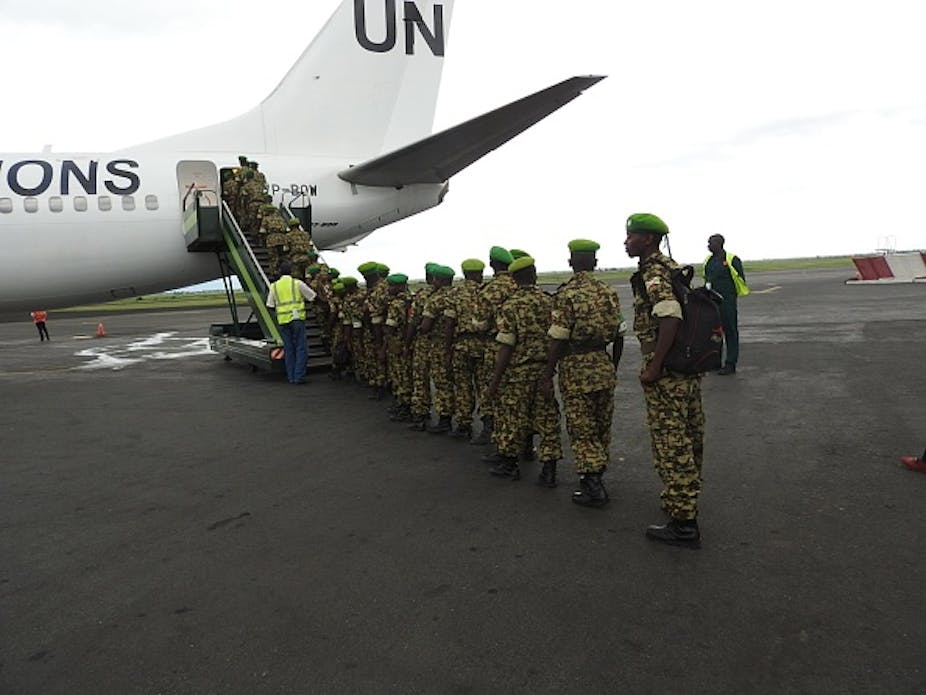 A line of men in military uniform board an aircraft with UN signage.