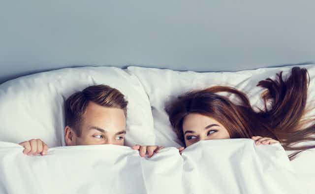 Young couple peeping from bedsheet on the bed at bedroom