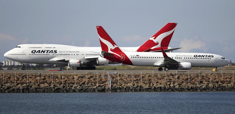 Two Qantas planes sitting nose to tail on a tarmac
